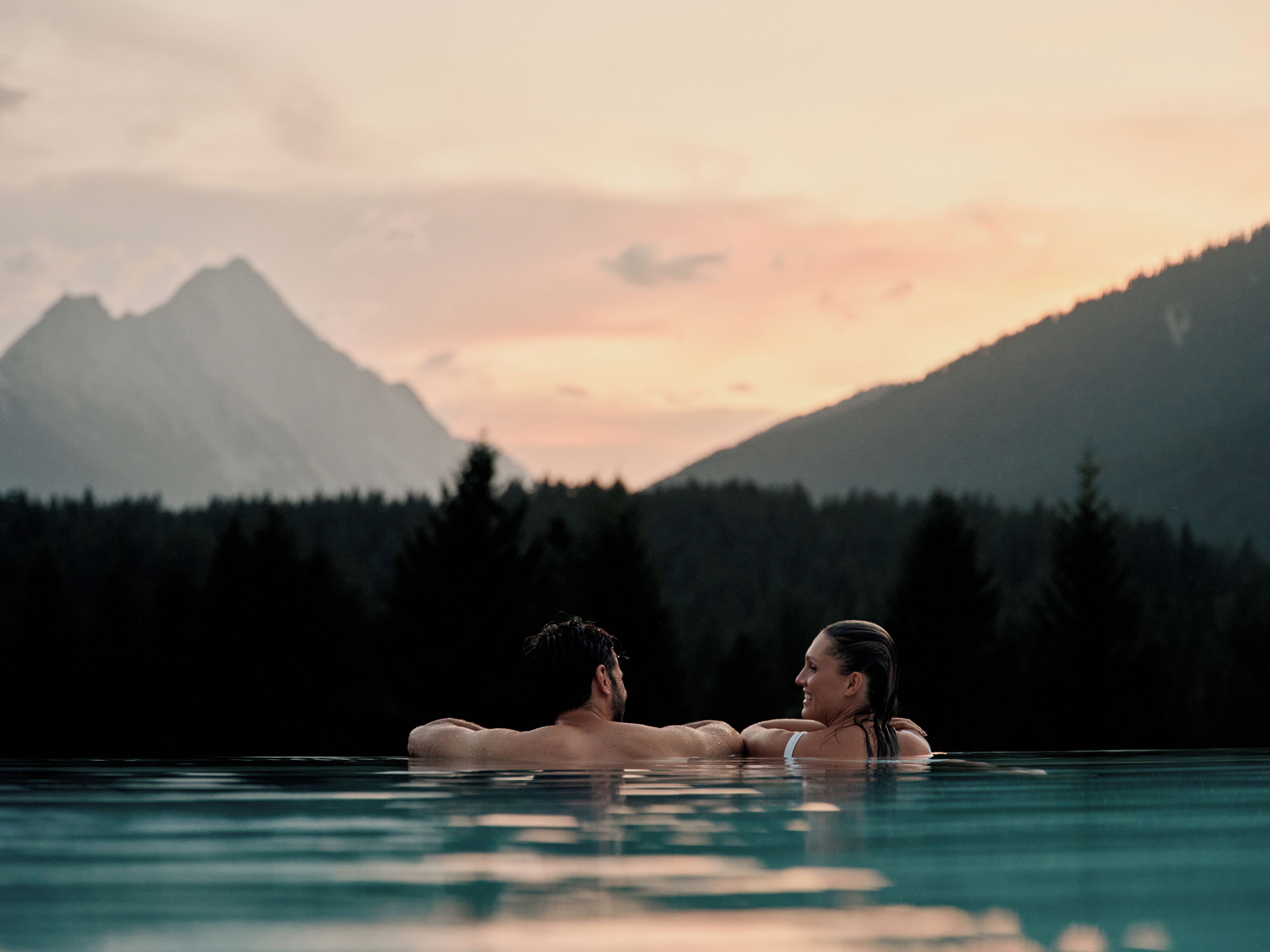 Una coppia in piscina, con un paesaggio montuoso sullo sfondo.