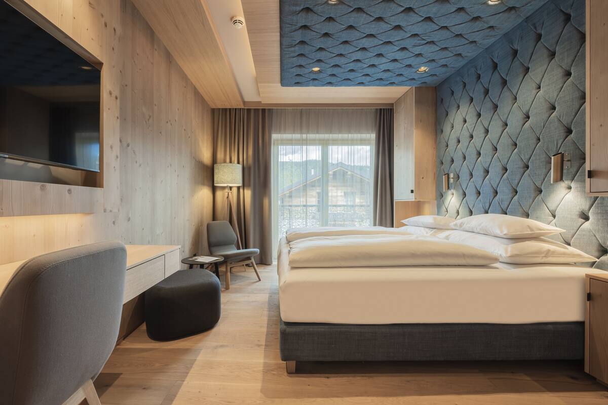 A modern hotel room with a large bed, a desk, a chair, and a view of the outside.