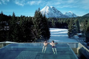An infinity pool with a view of a snow-covered mountain and forest. - Hotel Kristall (Leutasch)