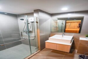 Un baño moderno con ducha envuelta en vidrio, un lavamanos con armario de madera y un espejo que refleja una puerta de madera.