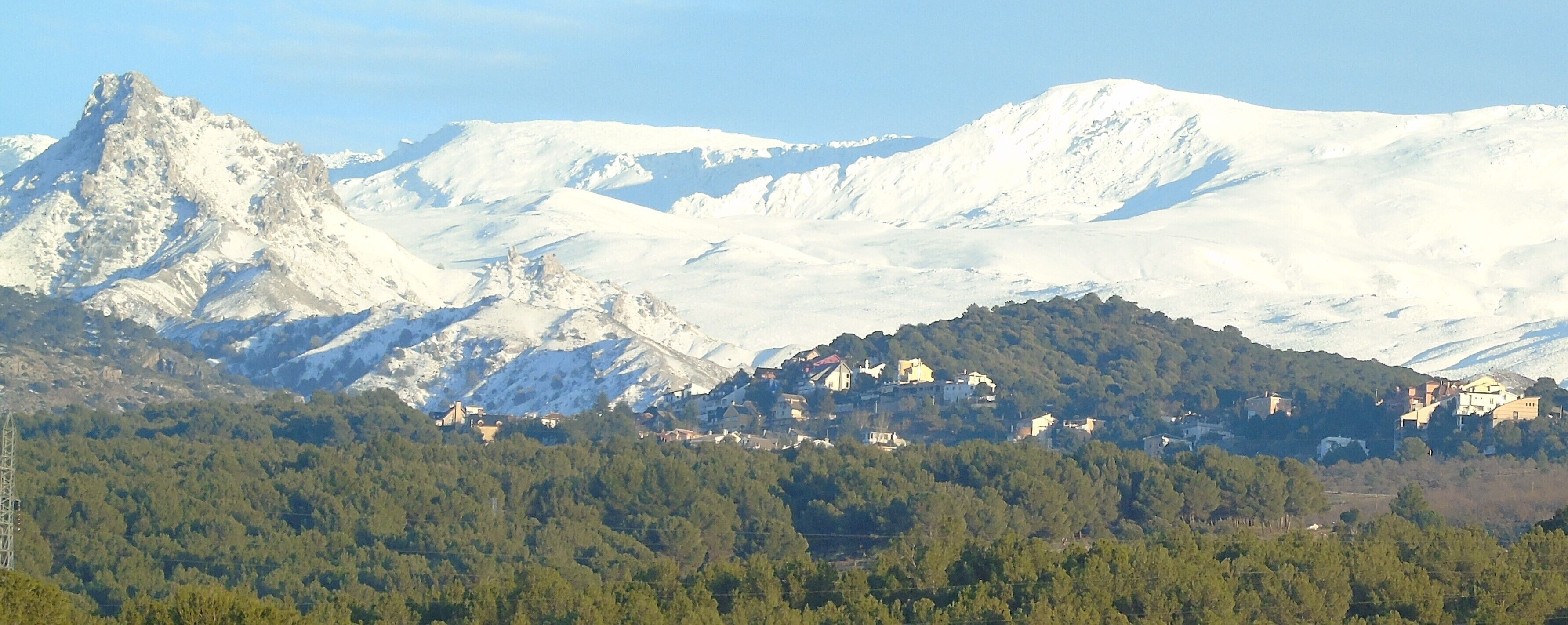 Een bergachtig landschap met besneeuwde toppen en een dorpje verscholen tussen de heuvels.