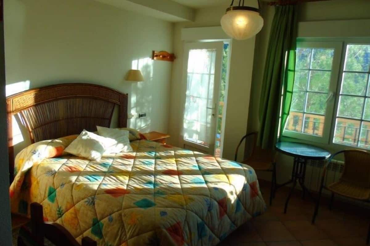 Une chambre à coucher avec un lit, une chaise, une table, une lampe et une fenêtre avec des rideaux.