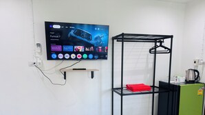 A hotel room with a TV mounted on the wall displaying various streaming services, a black metal drying rack with a red towel, and a green refrigerator. - K.L.Apartment (Rawai)