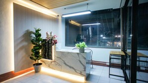 A modern reception area with a marble counter, potted plants, and a view of the city at night. - K.L.Apartment (Rawai)