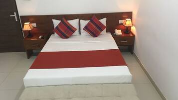 A neatly made bed with a red blanket, two bedside tables with lamps, and a headboard with two plaid pillows.