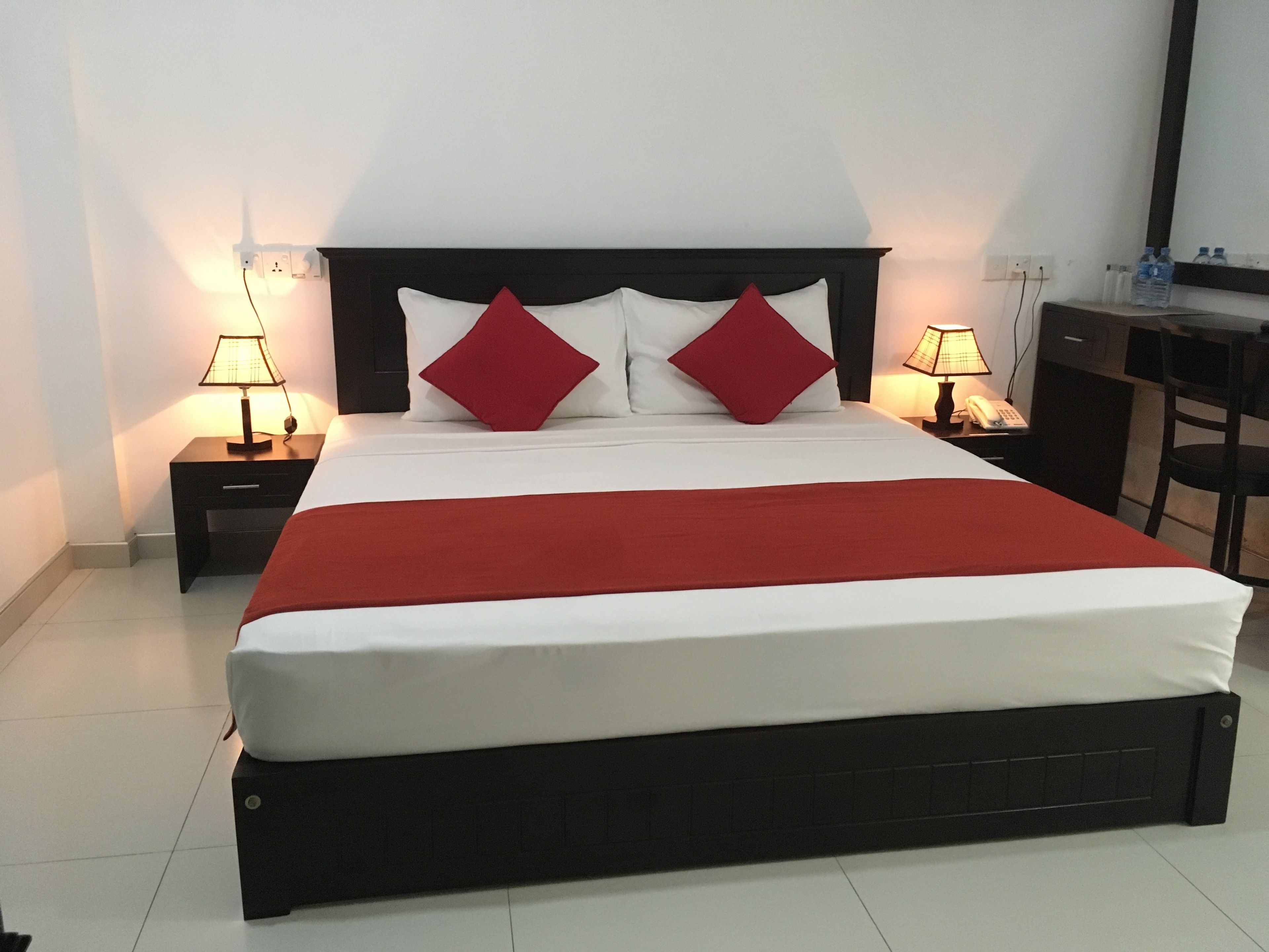 A neatly made bed with a red blanket, two bedside tables with lamps, and a desk with a chair.