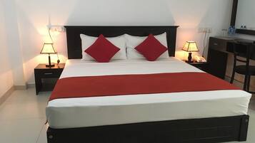 A neatly made bed with a red blanket, two bedside tables with lamps, and a desk with a chair.