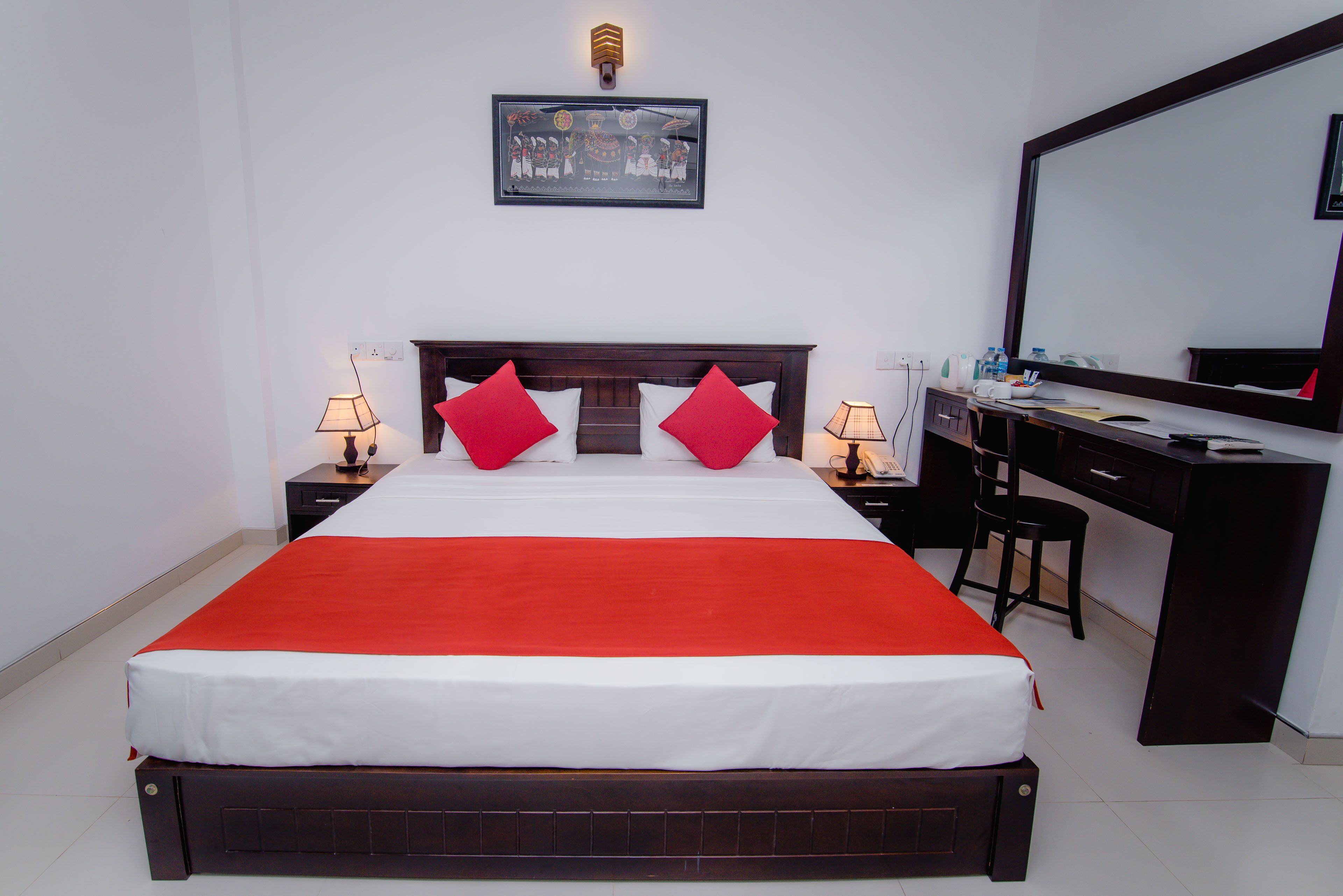 A neatly arranged bedroom with a bed, two bedside tables, a desk, and a large mirror.