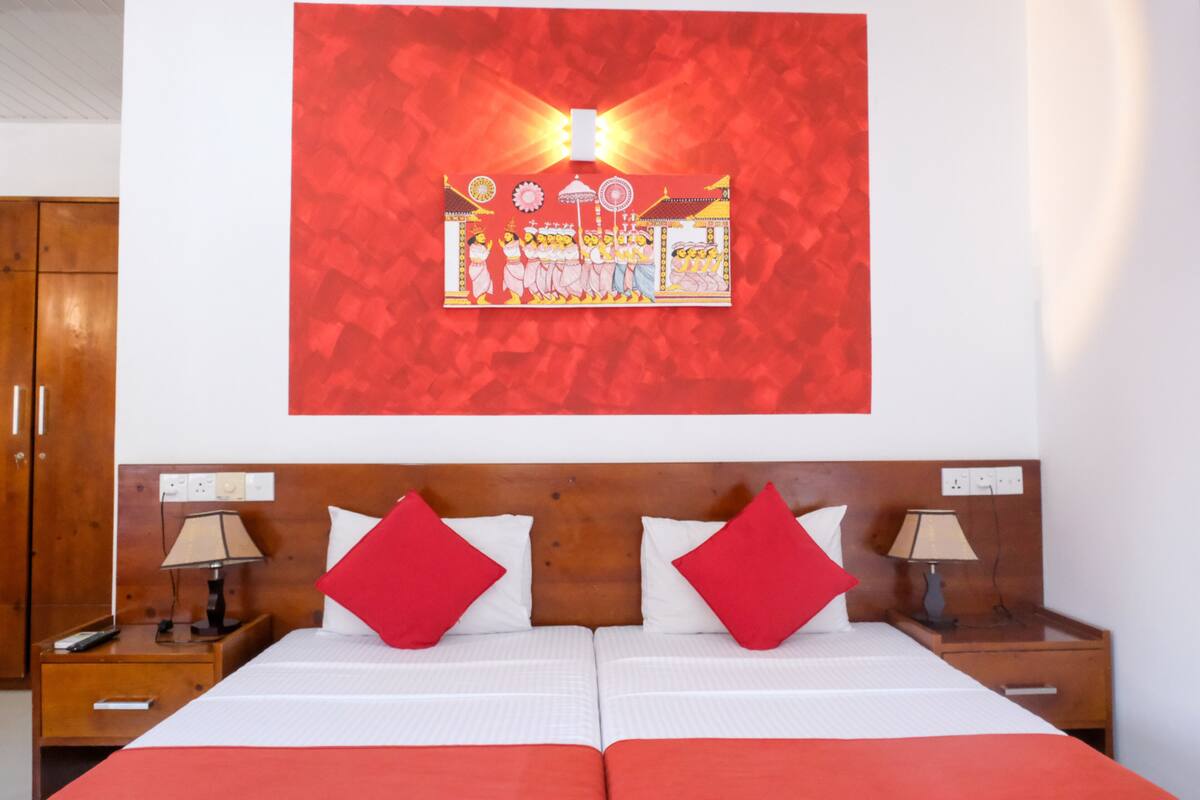 Ein Hotelzimmer mit einem großen Bett, zwei Nachttischen mit Lampen, einem hölzernen Kopfteil und einem roten abstrakten Gemälde an der Wand.
