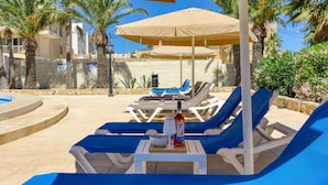 Un espace aménagé au bord de la piscine, avec des chaises longues, des parasols et une bouteille de vin.