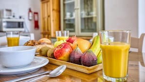 Une table en bois dressée pour le petit-déjeuner, avec un plateau de fruits, un verre de jus d’orange et un bol blanc.