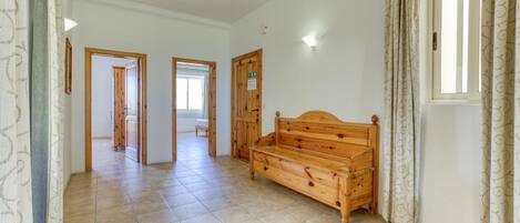 Una habitación amplia con un banco de madera, suelo de baldosas y una ventana con cortinas.