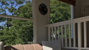 A porch with a beige sectional sofa, a white table, and a large wall clock. - Maison Jacaranda (Randburg)
