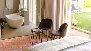 A modern bedroom with a large bed, a bathtub, a chair, and a small table. - Maison Jacaranda (Randburg)