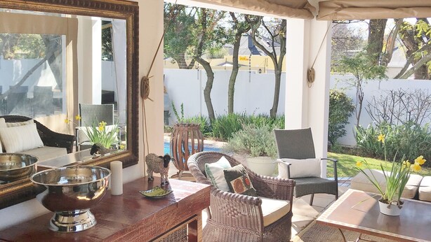 A sunlit patio with wicker furniture, a wooden table, and a large mirror reflecting the outdoor area. - Maison Jacaranda (Randburg)