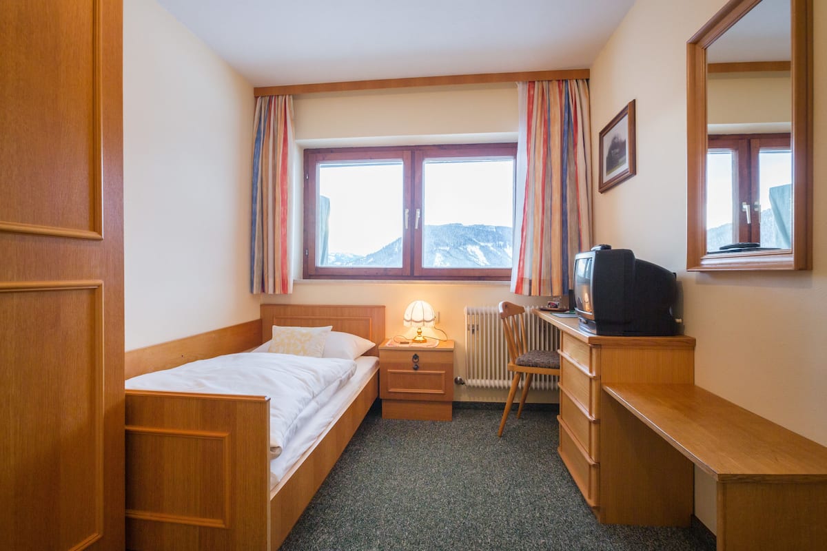 A hotel room with a bed, a desk, a chair, a lamp, a television, and a window with curtains.