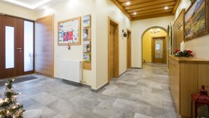 A hallway with wooden doors, a bulletin board, a radiator, a Christmas tree, and a reception desk with a painting. - Pension Roetelstein (Ramsau am Dachstein)