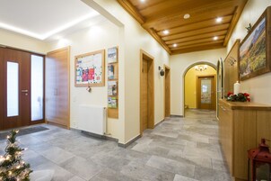 Un pasillo con puertas de madera, un tablón de anuncios, un radiador, un árbol de Navidad y una recepción con un cuadro.