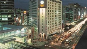 A multi-story building with a prominent sign on the corner, surrounded by other high-rise buildings and a busy street with moving traffic. - Brother Hotel (Taipei)