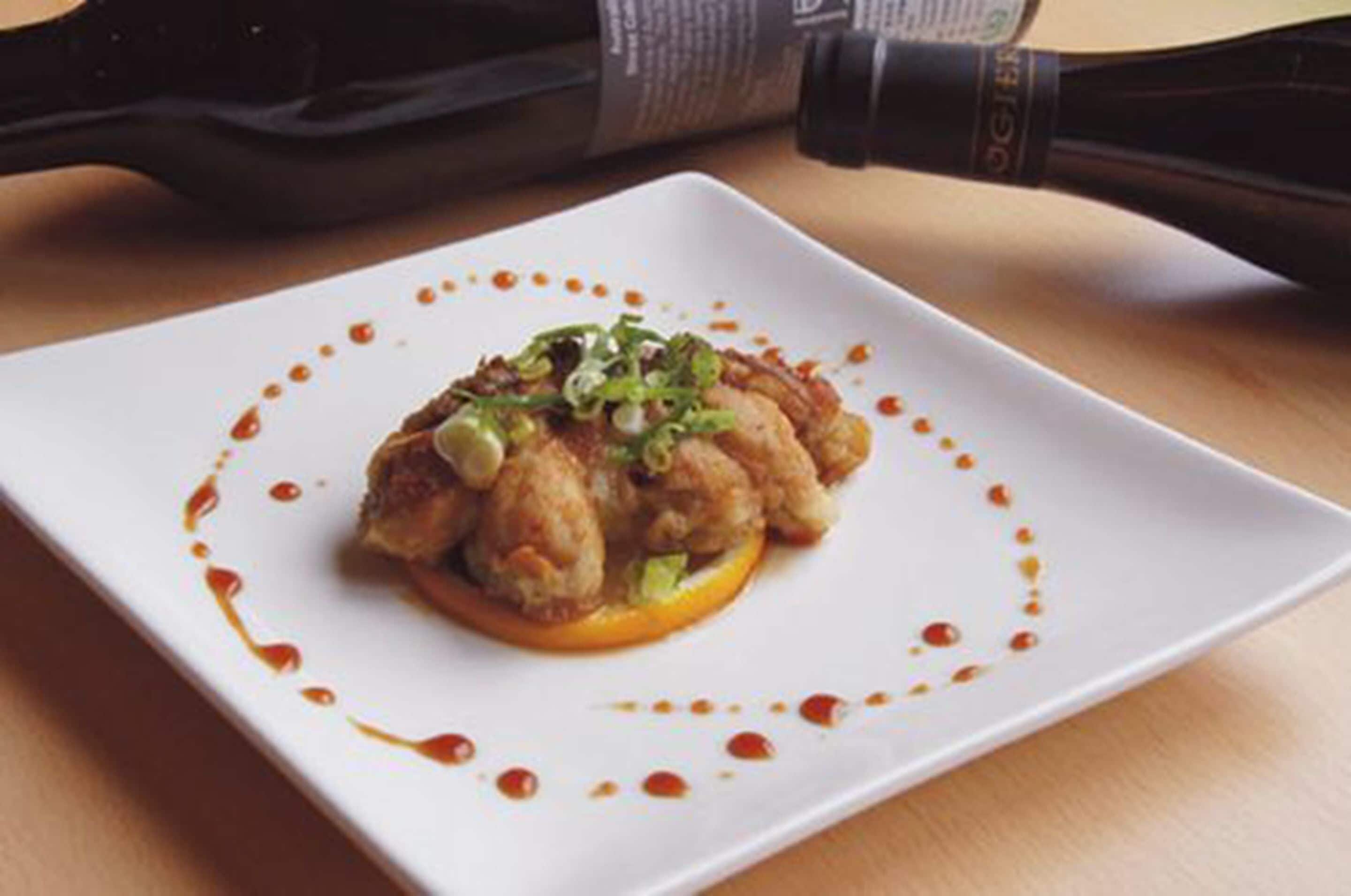 A square plate with a food item garnished with green onions, surrounded by a sauce pattern.
