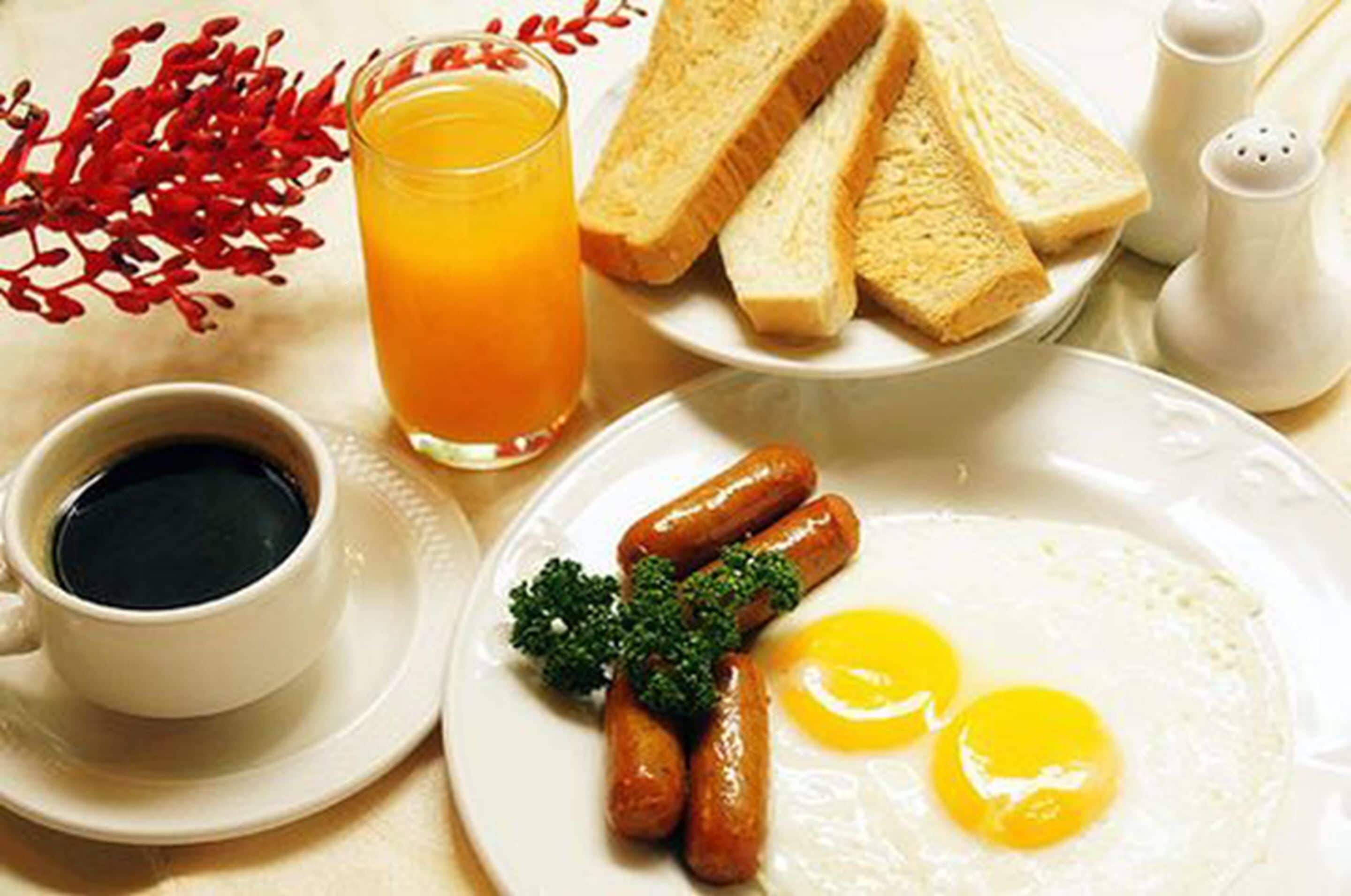 Un plato de desayuno con salchichas, huevos, tostadas y un vaso de jugo de naranja.