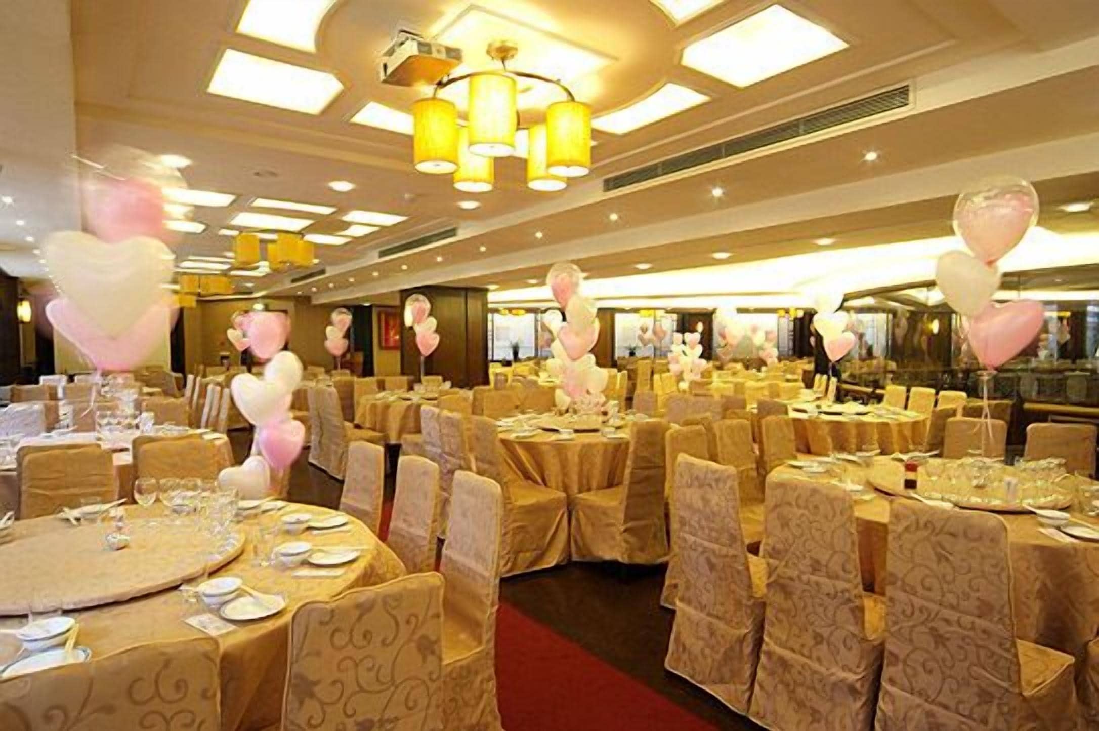 A banquet hall with round tables set for dining, covered with beige tablecloths and chairs with patterned covers.