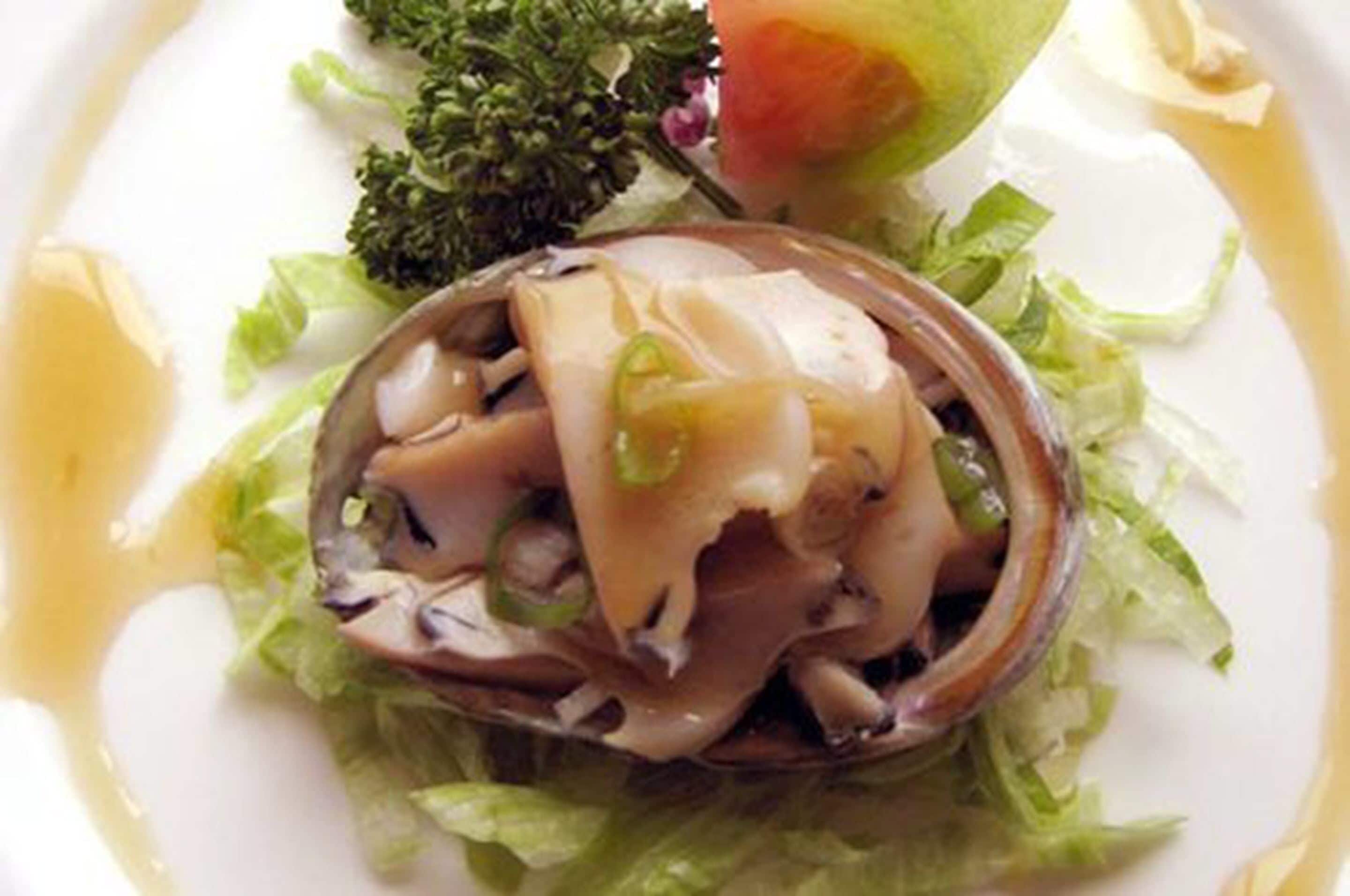 Um prato com prato de frutos do mar, possivelmente amêijoas, acompanhado de alface e uma fatia de tomate.
