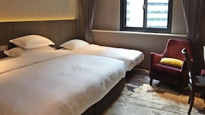 A hotel room with two beds, a red armchair, a large window with curtains, and a city view. - Brother Hotel (Taipei)
