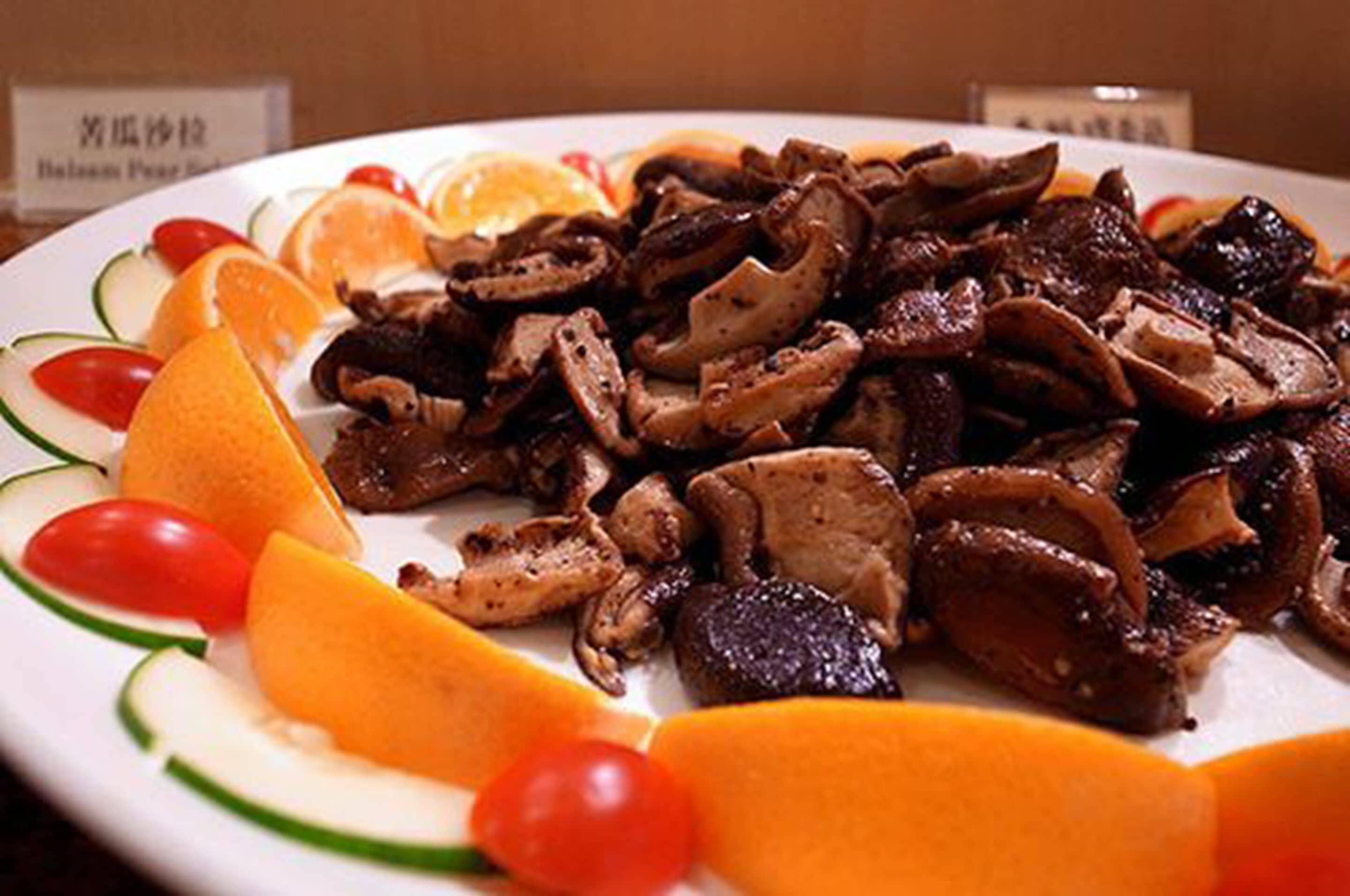 A plate of cooked mushrooms and sliced fruits.
