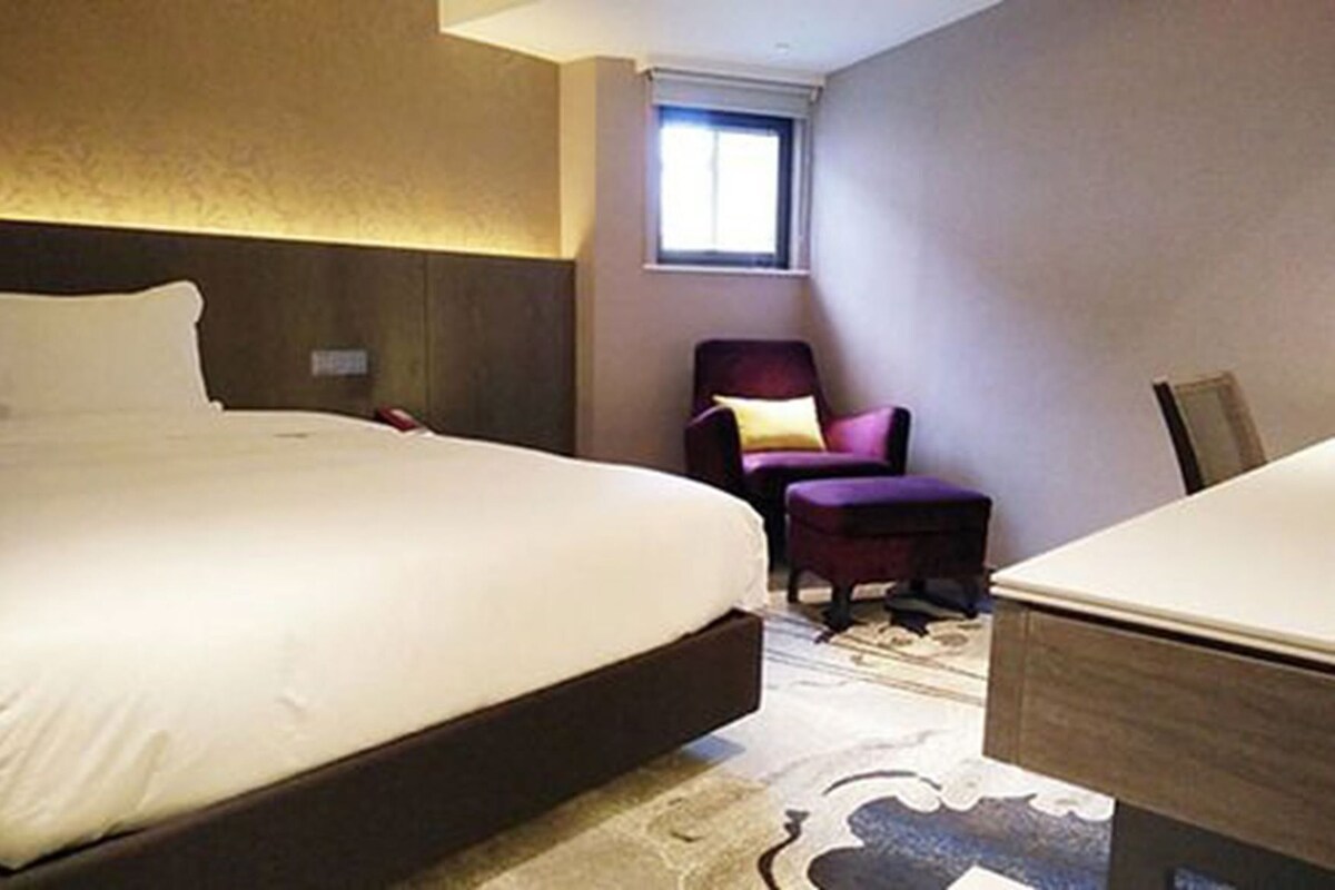 A hotel room with a large bed, a chair, and a small table.