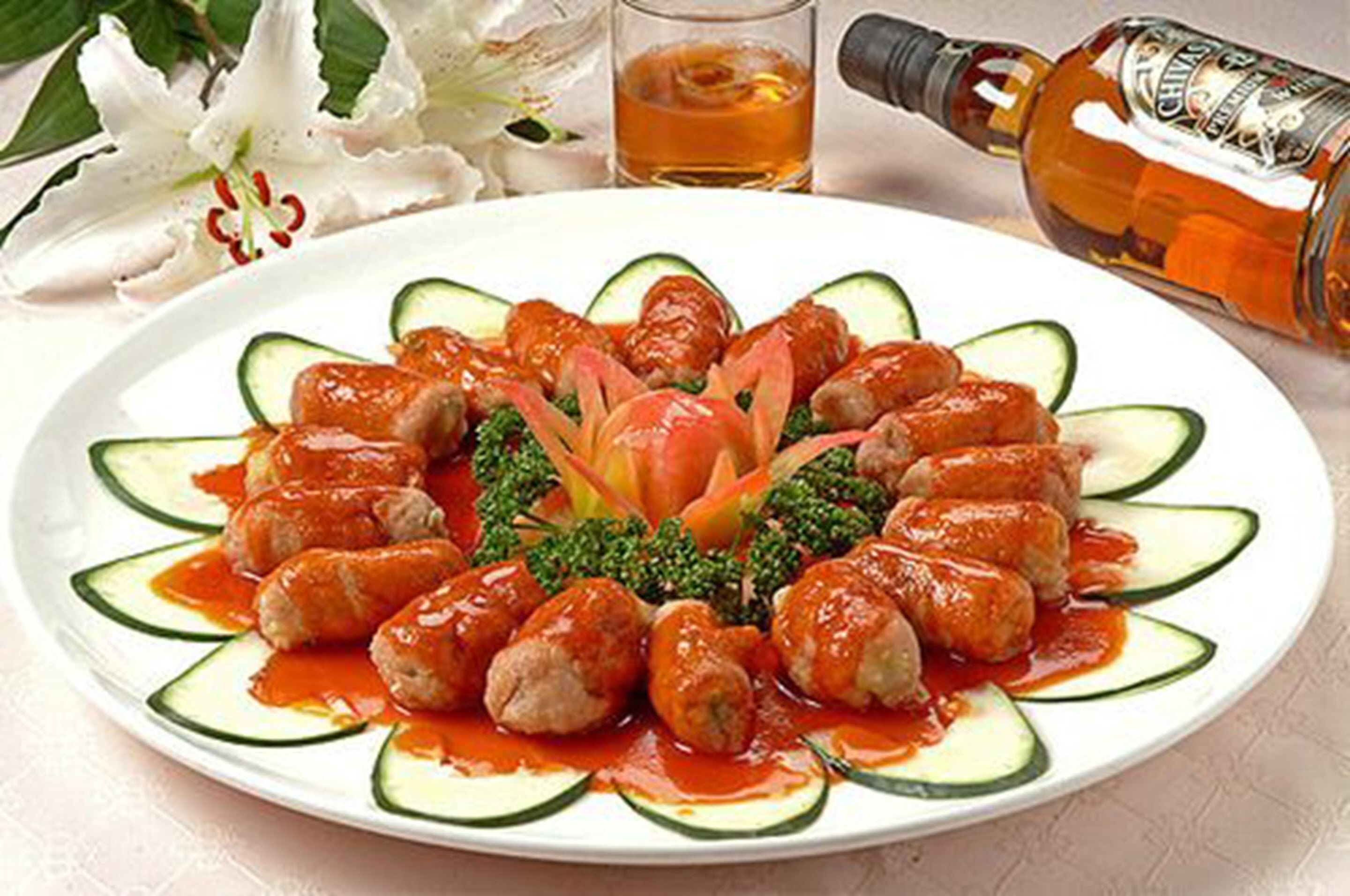 Ein Teller Hackbällchen mit Soße und Gurkenscheiben, die als Blumenmuster angeordnet sind.