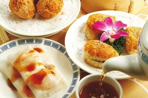 Een tafel met borden eten, waaronder dumplings en broodjes, en een theepot die thee schenkt.