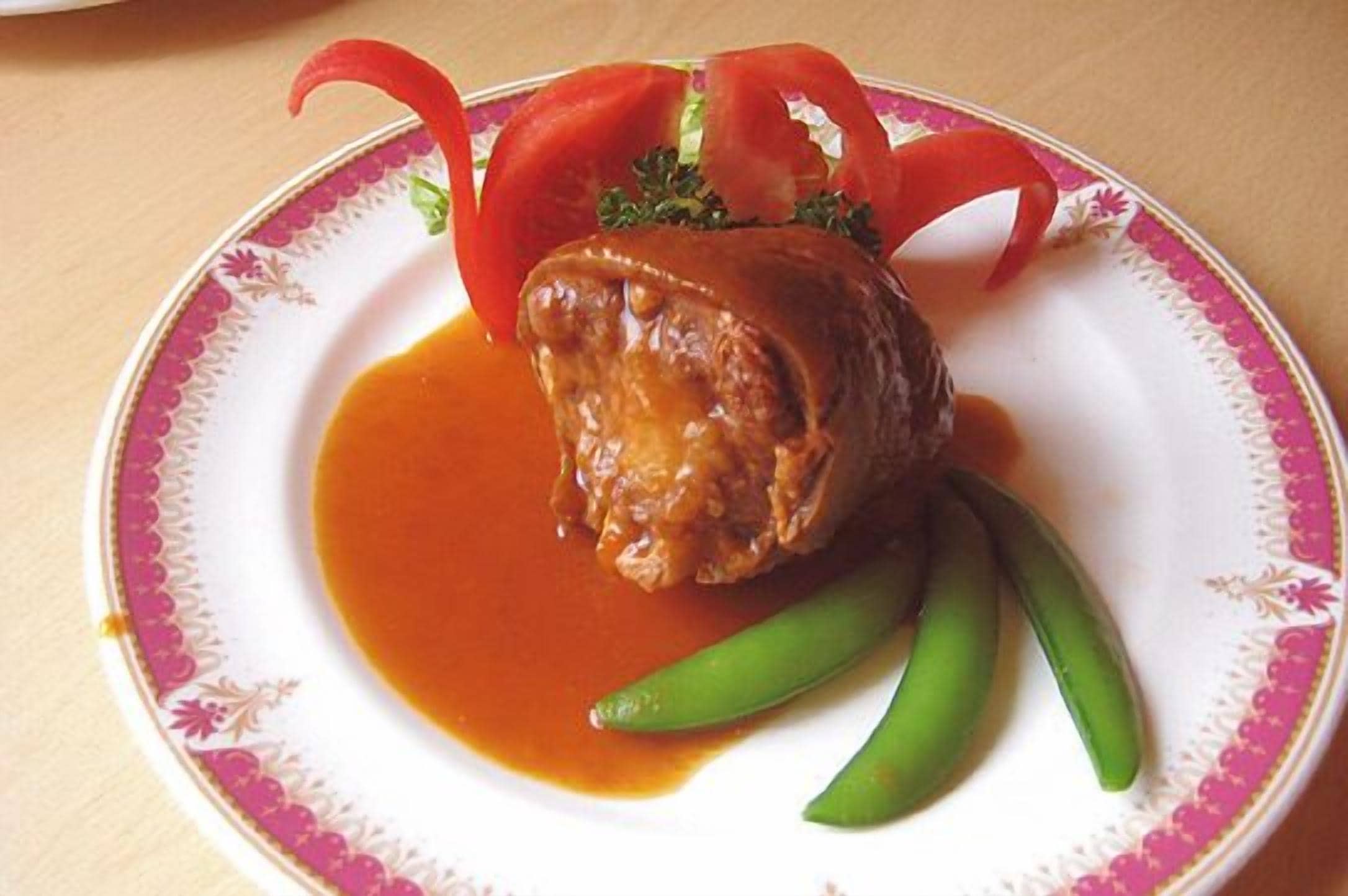 A plate with a meat dish, green beans, and red bell pepper slices.