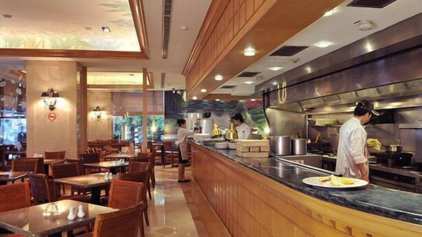 A modern restaurant with wooden furniture, a marble counter, and a chef preparing food. - Brother Hotel (Taipei)