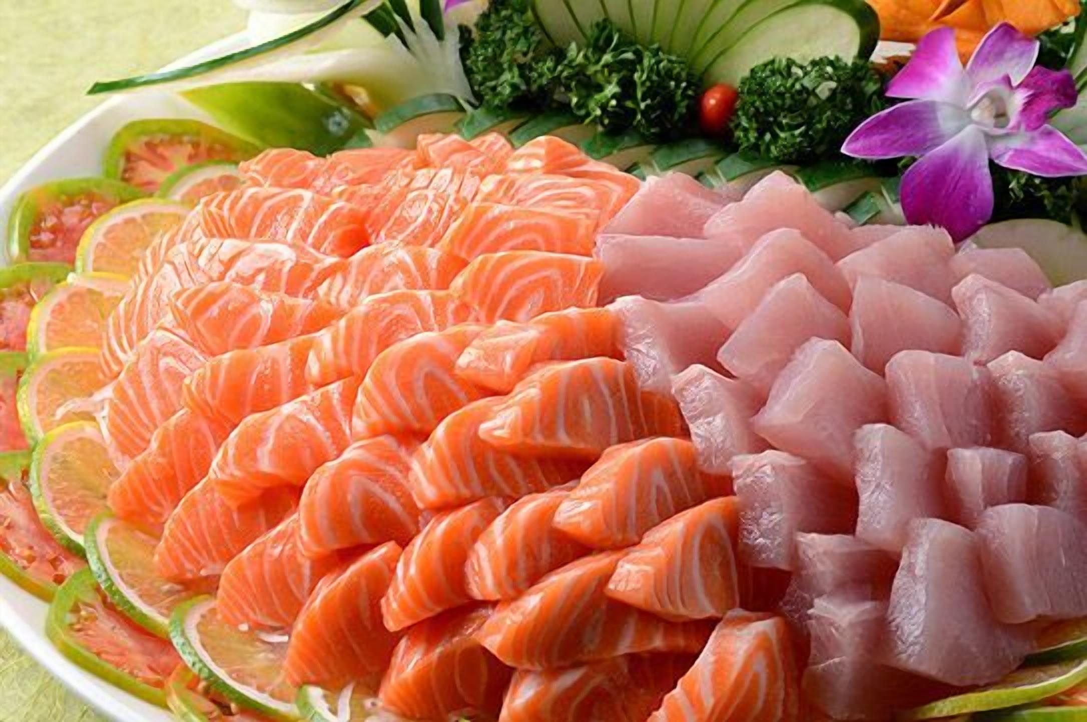 A plate of sushi with salmon and tuna, garnished with cucumber and a purple flower.