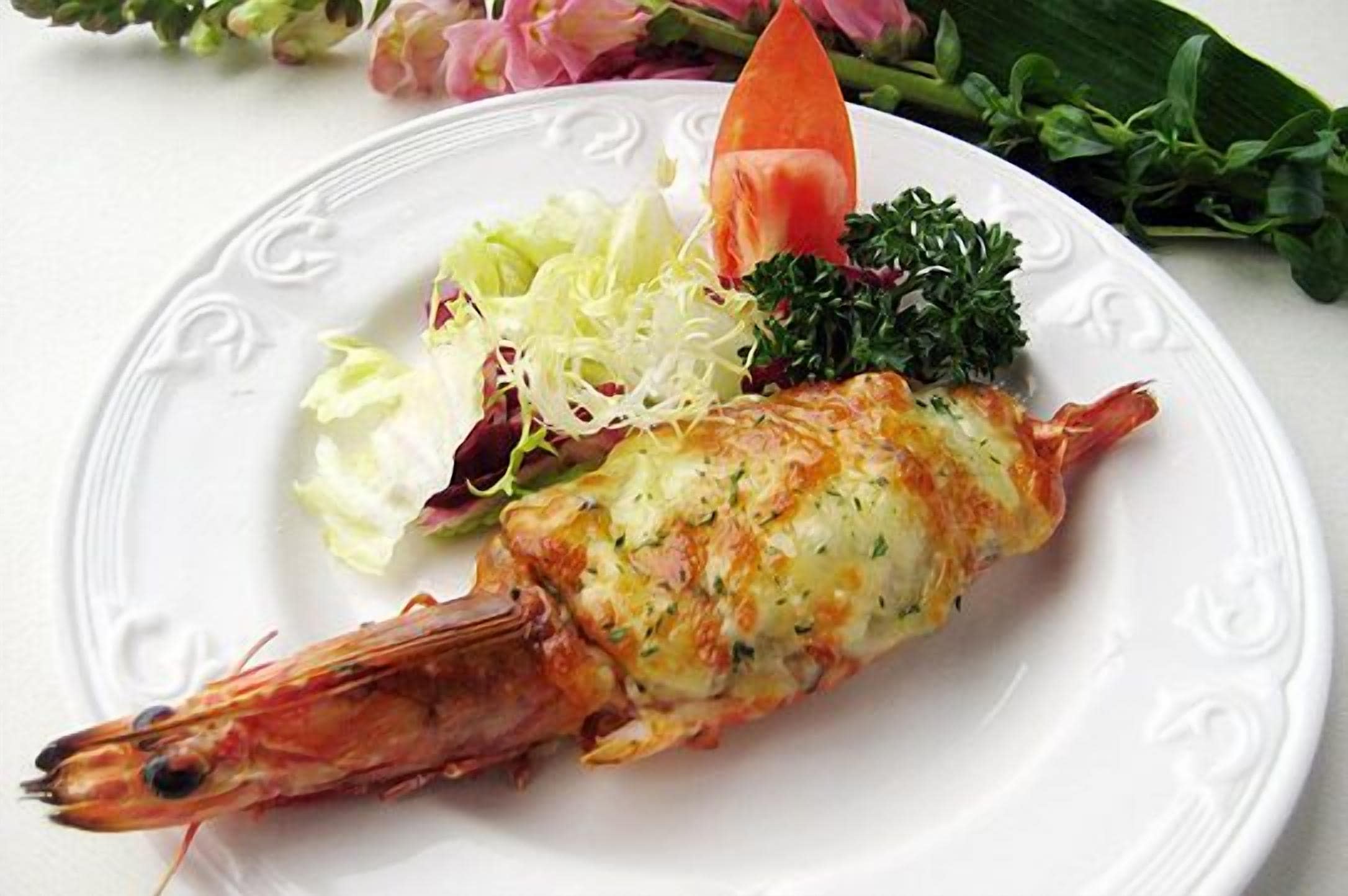 A plate with a cooked shrimp, a slice of tomato, and a side salad.