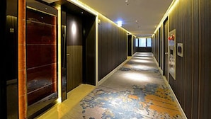 A long, narrow hallway with a patterned carpet, wooden walls, and a glass elevator. - Brother Hotel (Taipei)