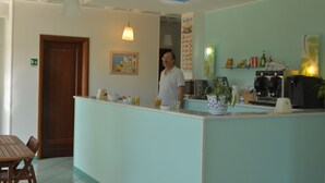Zona de recepción de un hotel con una puerta de madera, una barra con una cafetera y una planta en maceta.