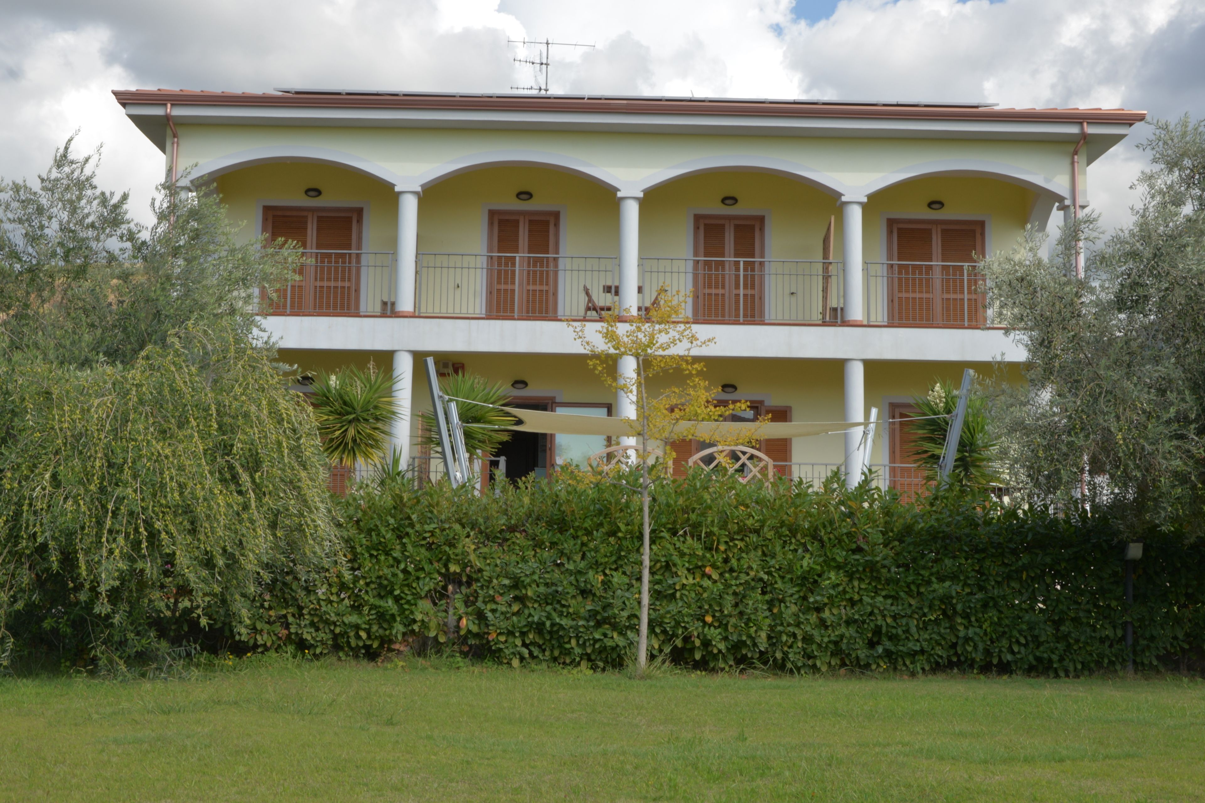 A two-story building with a balcony on the upper floor, surrounded by greenery.