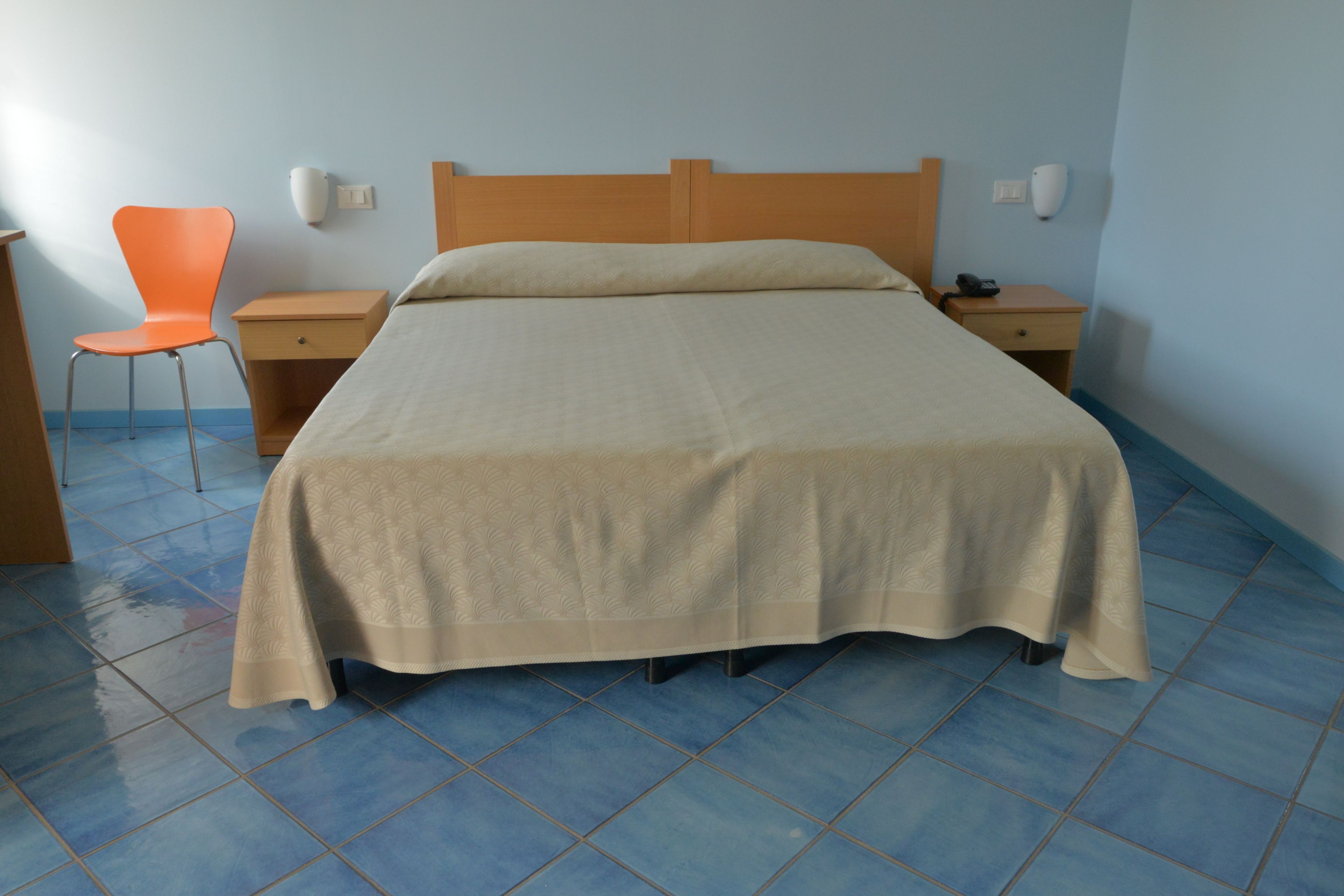 A bedroom with a bed, a chair, a nightstand, and a wall-mounted phone.