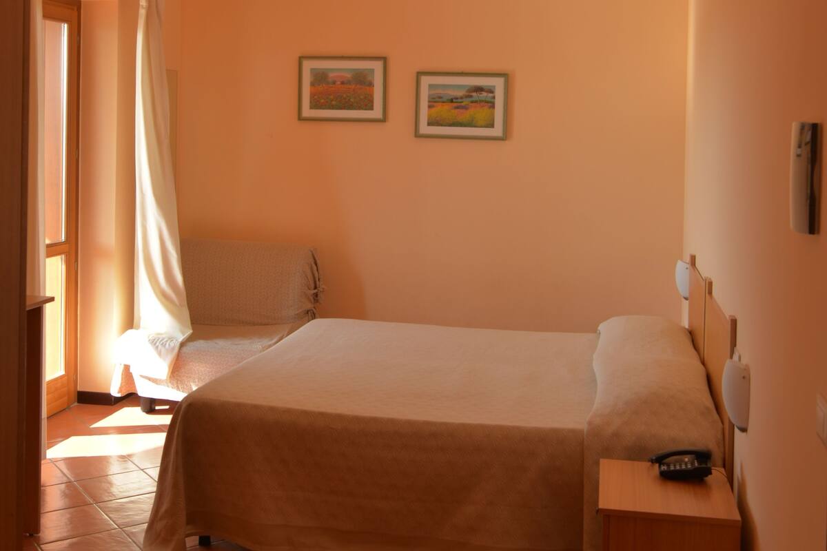 Un dormitorio con una cama, una mesita de noche, una lámpara colgante y dos cuadros en la pared.