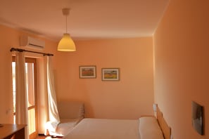 A bedroom with a bed, an air conditioning unit, a desk, and two framed pictures on the wall. - Larus Hotel (Sangineto)