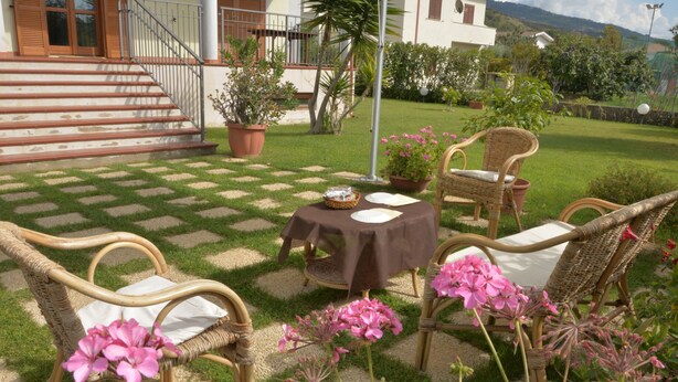 Un patio con mobiliario de mimbre, una mesa cubierta con tela y plantas en macetas.