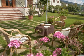 Une terrasse dotée de meubles en osier, d’une table recouverte d’une nappe et de plantes en pot.