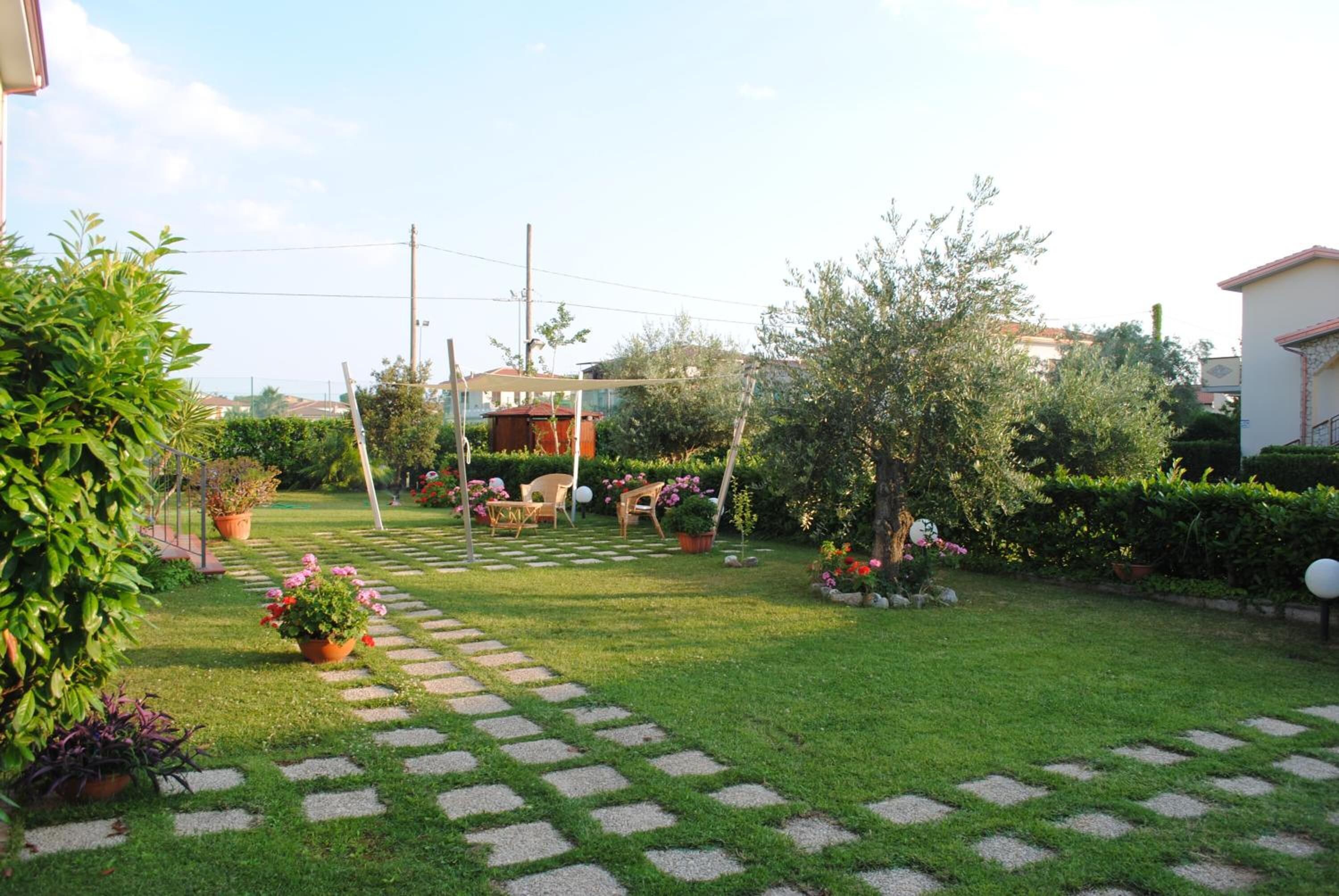 Un jardín bien cuidado con un sendero de piedra que lleva a una zona de estar, rodeado de abundante vegetación y plantas en macetas.