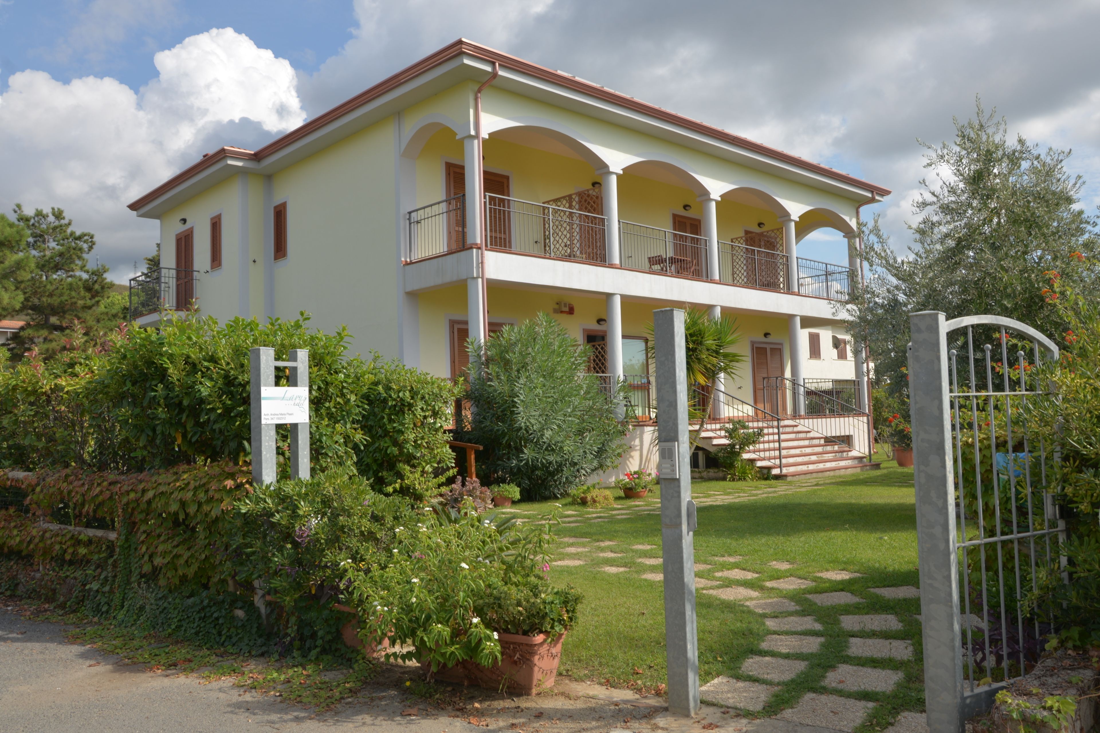 Ein zweistöckiges Gebäude mit Balkon, einer Treppe zum Eingang und einem gepflegten Garten.
