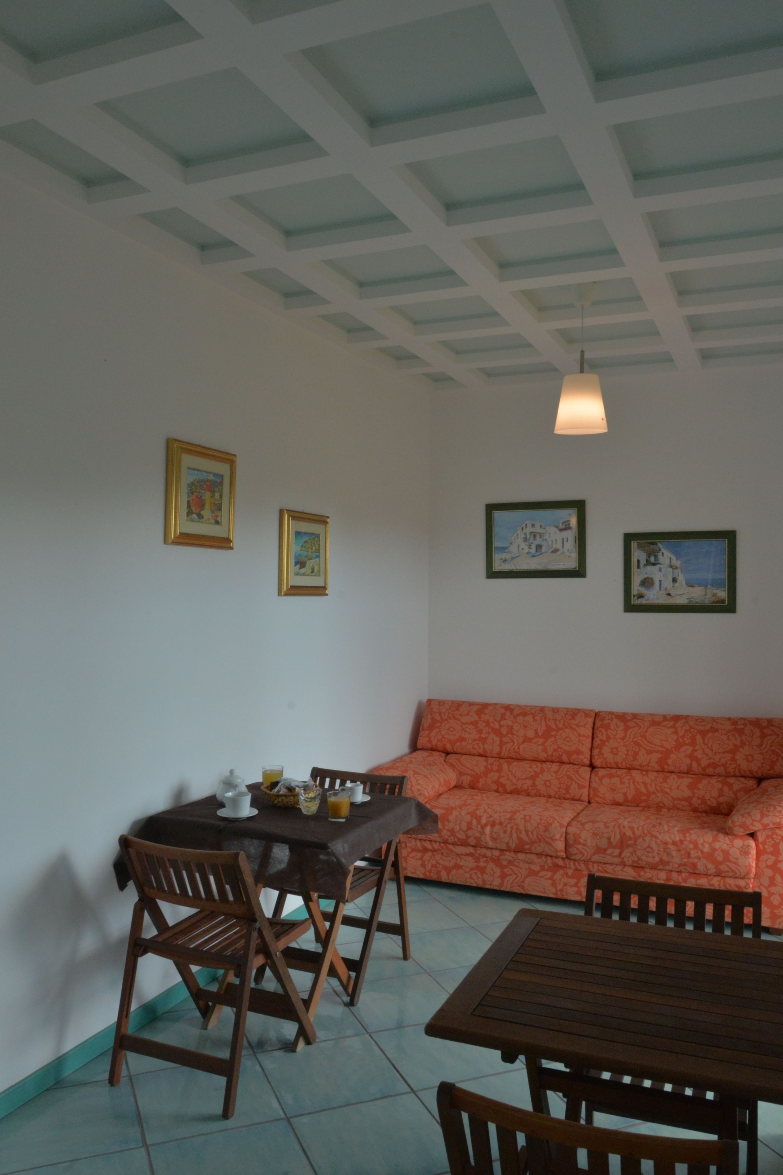 A dining area with a wooden table and chairs, a sofa, and framed artwork on the walls.