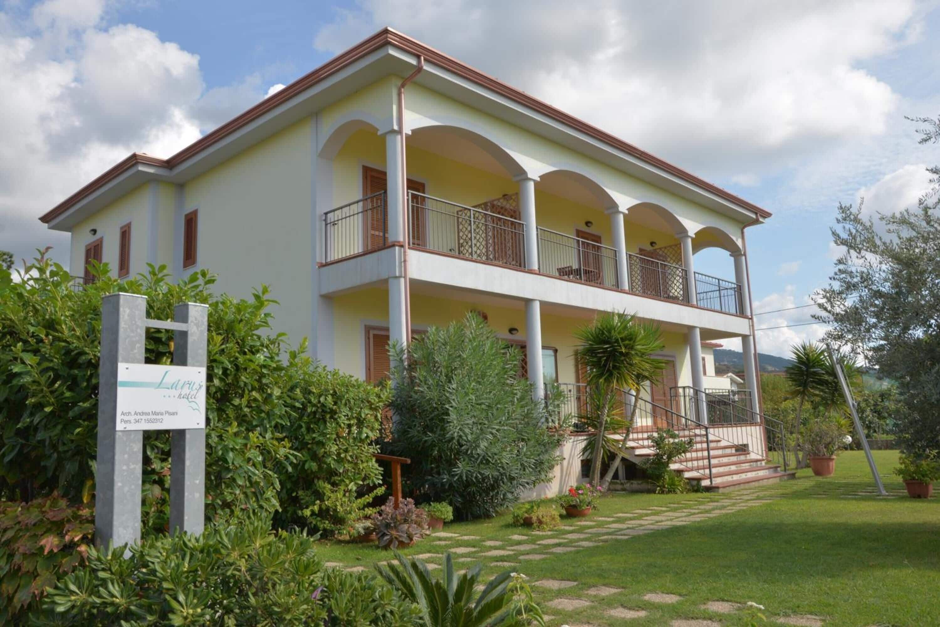 A two-story building with a balcony on the upper floor, surrounded by greenery and a well-maintained lawn.