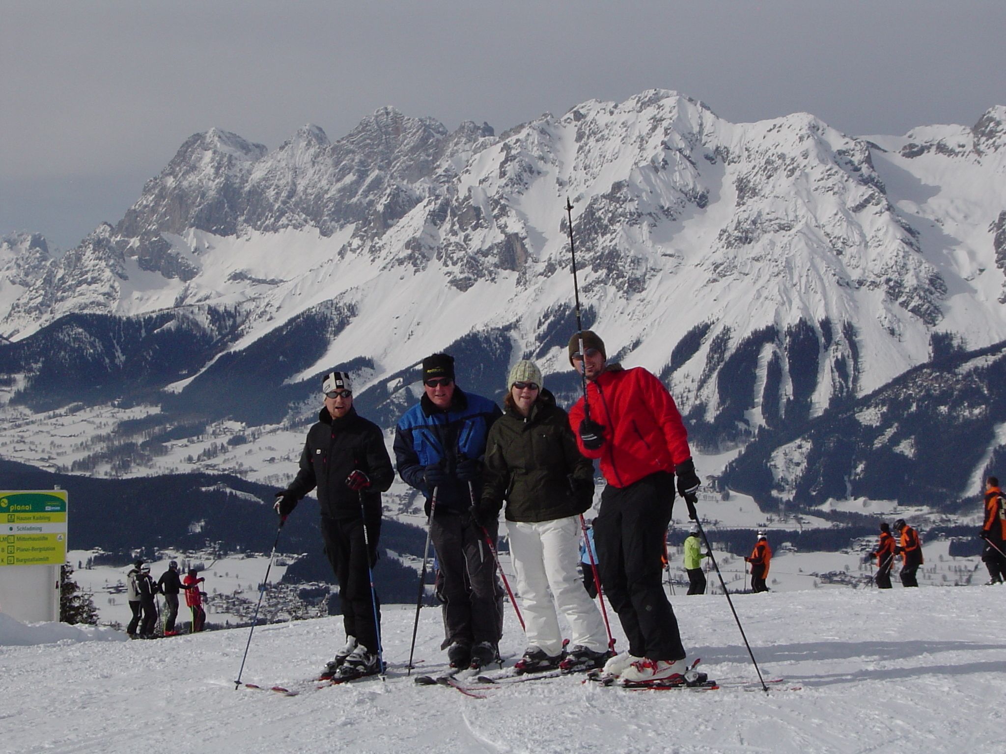 A group of people on skis on a snowy mountain with a sign indicating ski trails.