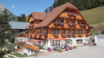 Ein traditionelles Holzchalet mit mehreren Balkonen, die mit Blumenkästen geschmückt sind, einem überdachten Sitzbereich im Freien und Blick auf die umliegenden Berge.